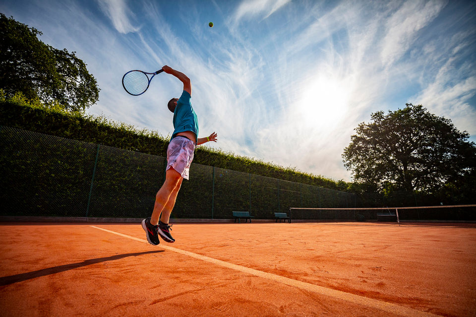 man jumping to serve in a tennis match on a summers day