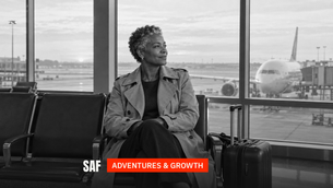 A woman in her 50s at an airport gate at dawn with her carry-on, looking out at a plane.