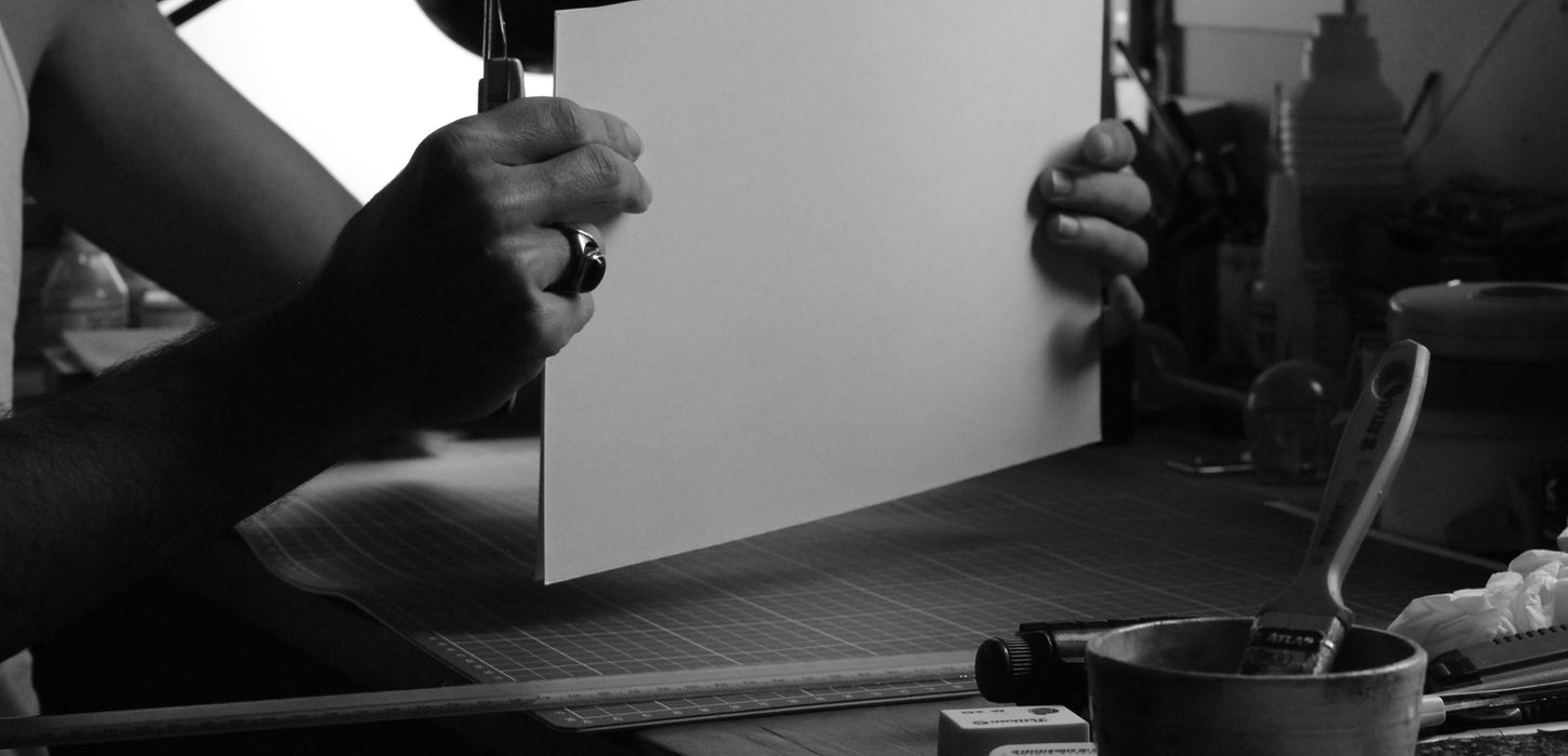 Foto de Santangelo em seu ateliê segurando folhas tamanho A4 para serem cortadas.