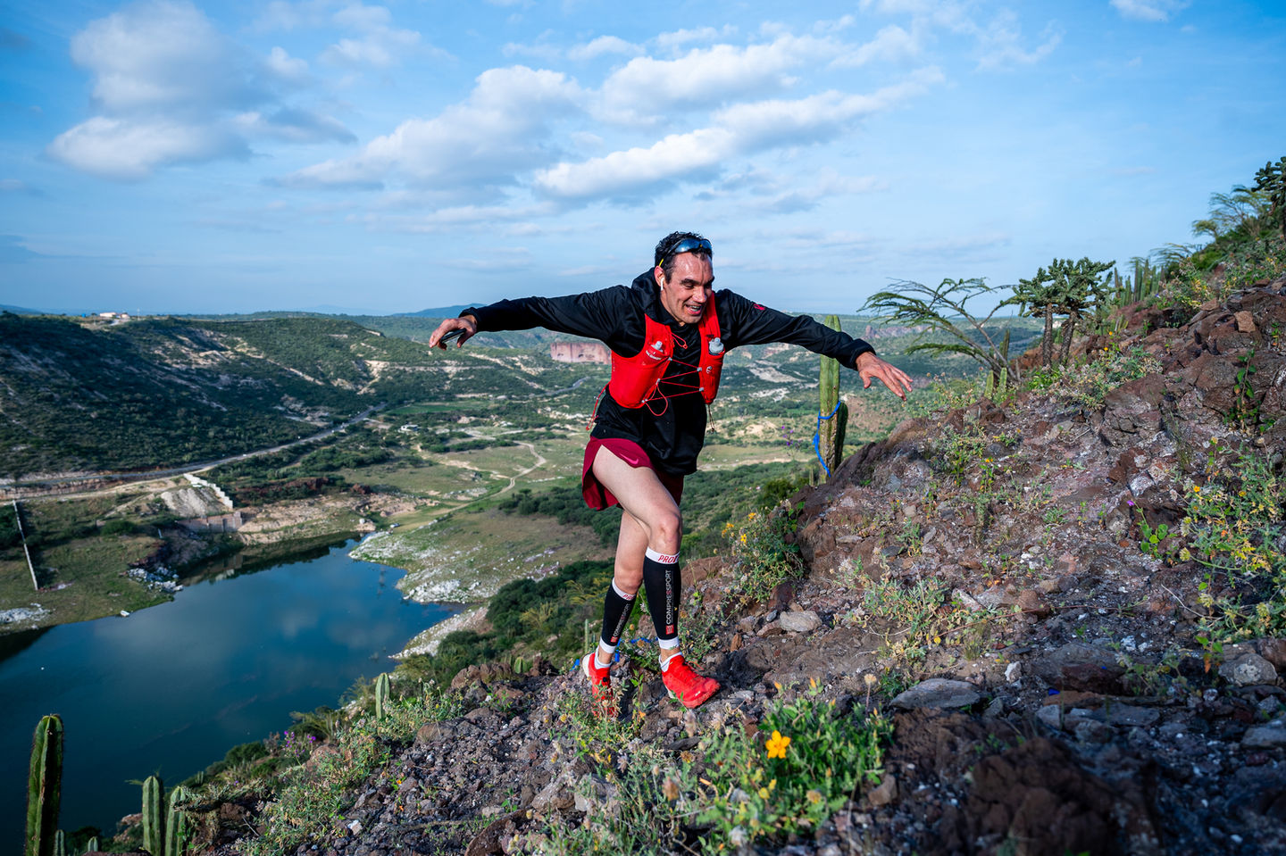 Hombre sonriendo y corriendo en las montañas, fondo del lago, cielo azul. Catiri Media.