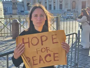 Yona Tukuser holds a "HOPE FOR PEACE" sign in St. Peter's Square at the Vatican during the Conclave