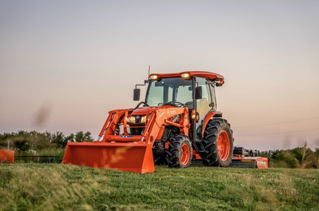 Kubota utility tractor with front loader mowing a large field at dusk in Southern California