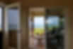 Interior view through an open swinging screen door to a covered porch with a person enjoying an ocean view