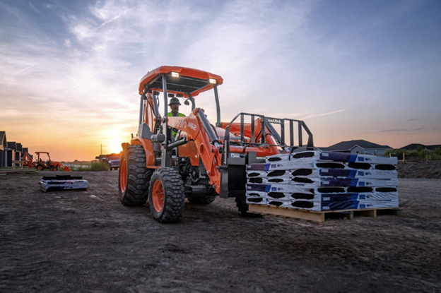 Kubota TLB tractor loader backhoe moving pallets of materials at a California construction site at sunset