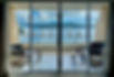 Interior view through clean glass doors to a balcony overlooking water with white cockatoos perched on the railing