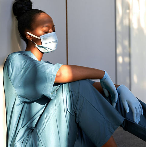 Black woman in medical scrubs sitting with eyes closed, expressing exhaustion and burnout common among Sinai employees