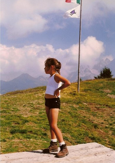 Young Luana standing on an Italian mountain top as a child, the Italian flag flying behind her