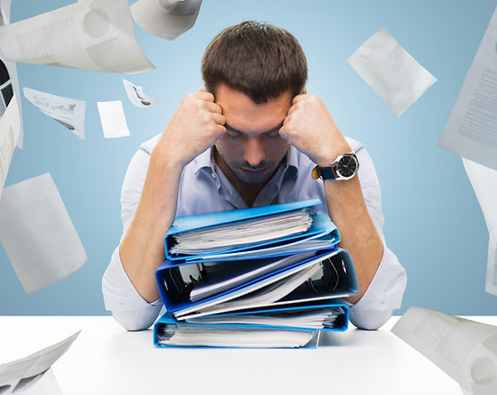 gestresseter Geschäftsman vor einem Stapel Ordner voller Dokumente