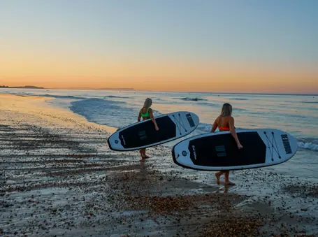 two women carrying surfboards on a beach