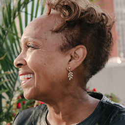 Smiling woman with short curly hair. Only the side of her face is showing, and she is wearing gold, leaf stud earrings.