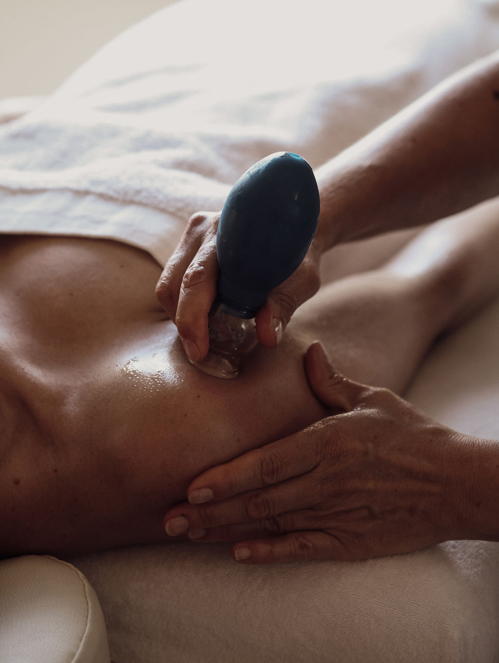 Close-up van een vrouw, liggend op de rug, die cuppingtherapie ondergaat. De setting is ontspannend en rustgevend.