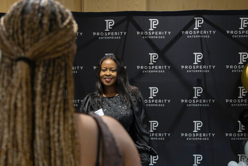 Woman posing in front of a branded event backdrop while another person stands in the foreground.
