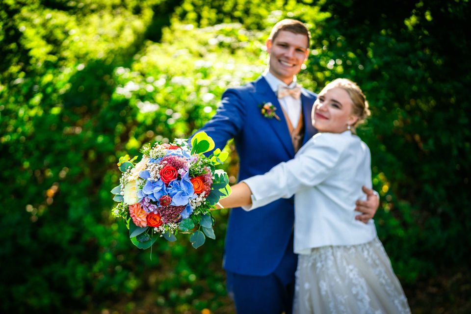 Hochzeitspaar mit buntem Brautstrauß, festlich gekleidet, strahlend glücklich bei ihrer Feier in den Lenderstuben Balzhausen.