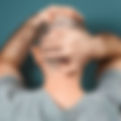 A man facing a wall. He is wearing a grey tshirt and has very short dark hair. He has his arms up with one hand grasping the back of his hand and one up on top of his head. You can't see his face.