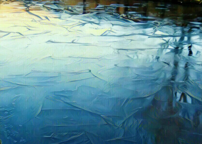 Cracked blue-white ice on frozen water, with mirrored reflections and a calm, chilly winter scene.