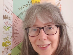 a smiling middle aged woman standing in front of a flower remedy wall poster