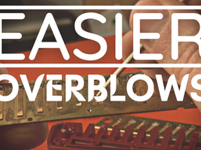 Close up of hands holding a harmonica reed plate, cleaning it with a cocktail stick. TEXT IN FRONT: EASIER OVERBLOWS