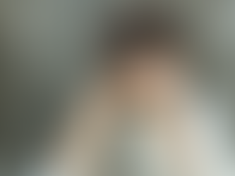 Child playing harmonica, wearing hat, shirt and suspenders, in front of wooden fence.