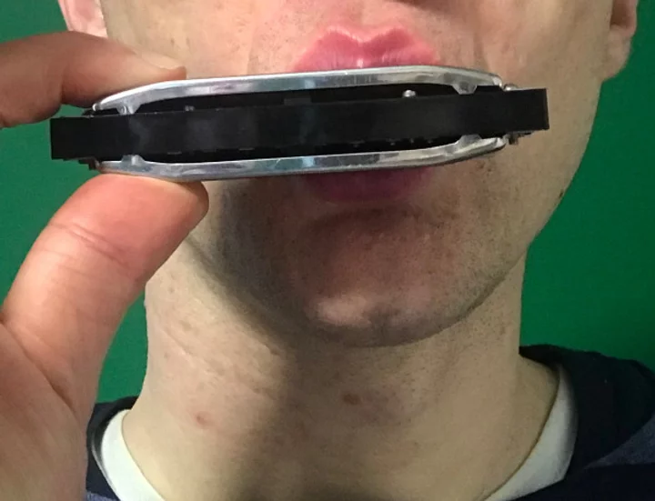 Photo of a close up of a man's mouth covering a harmonica