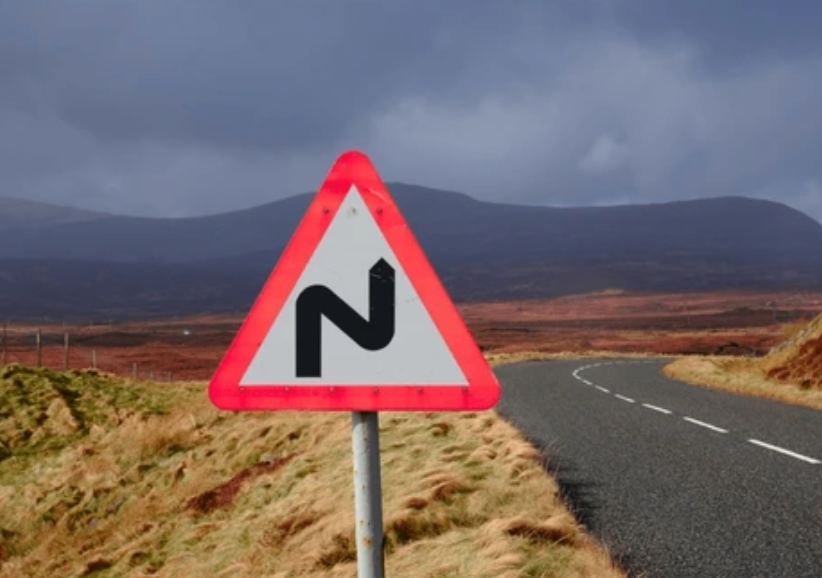 Road sign showing bend ahead, in front of mountains and dark cloudy sky.