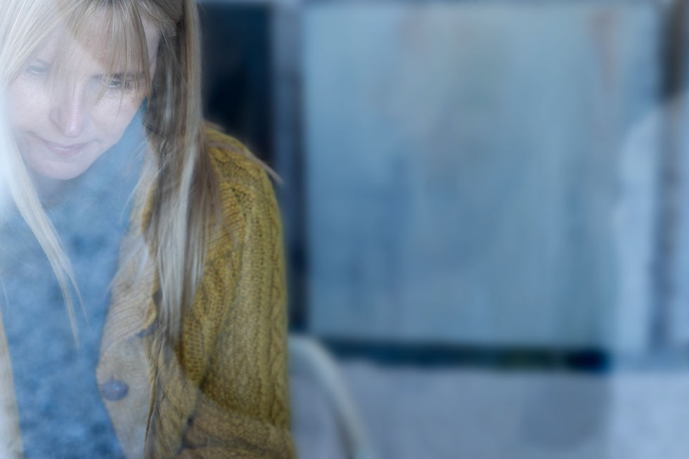 A woman in a yellow sweater looks down, surrounded by a soft blur, creating a tranquil mood. Blue and gray tones fill the background.