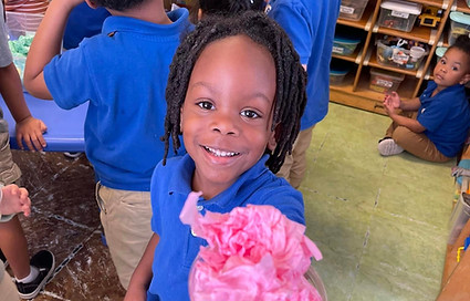 Child holding up pink paper flower, smiling