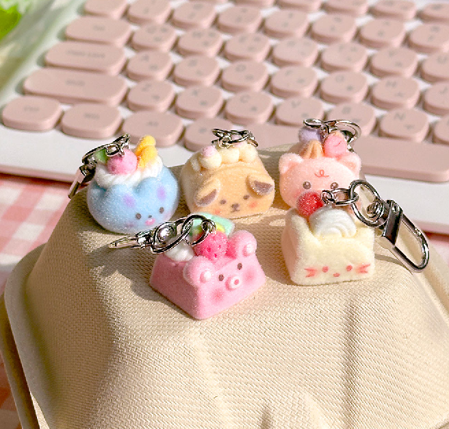 Display of five pastel cake keyrings arranged on a beige pouch.