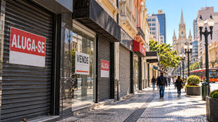Fachadas de lojas fechadas em uma rua comercial de Curitiba, com placas de venda e aluguel de imóveis.