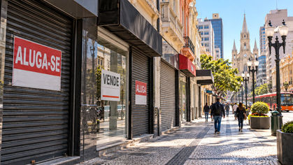 Fachadas de lojas fechadas em uma rua comercial de Curitiba, com placas de venda e aluguel de imóveis.