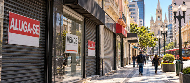 Fachadas de lojas fechadas em uma rua comercial de Curitiba, com placas de venda e aluguel de imóveis.