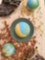Bombe de bain fraîcheur d'été jaune, vert et bleu posée sur socle vert sur planche et copeaux, entourée d'autres boules