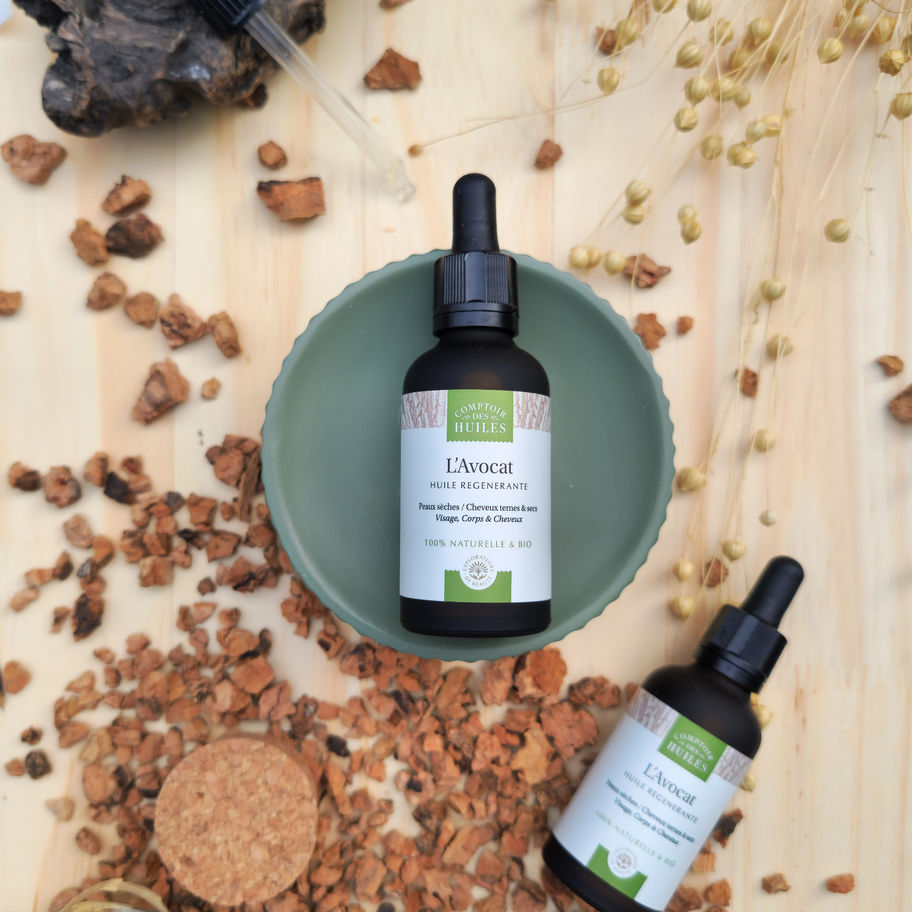 Une huile en verre est posée sur un support pour la mettre en valeur, il y a une pipette à côté et une autre huile.