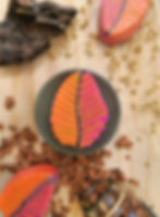 Bombe de bain feuille d'automne parfum pêche, cassis et framboise sur socle vert entourée de bombes feuilles orange et rose