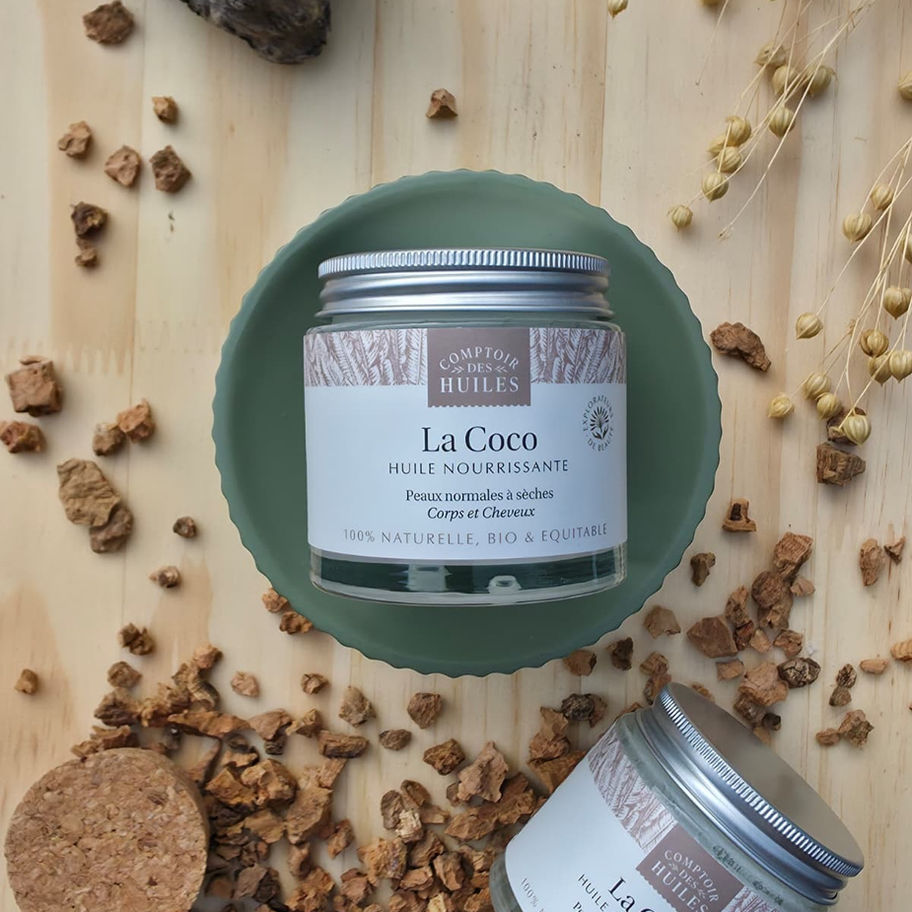 Pot d'huile de coco bio fermé posé sur un socle vert d'eau avec des copeaux de bois