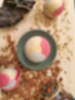 Bombe de bain tulipe posée sur socle vert sur une planche en bois et copeaux, entourée des boules rouges, jaunes et blanche