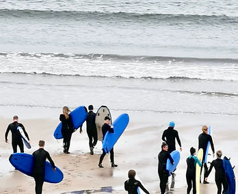 Primary School tour heading into sea during a lesson with Celtic Surf School in the water at Spanish Point beach, County Clare, Ireland.