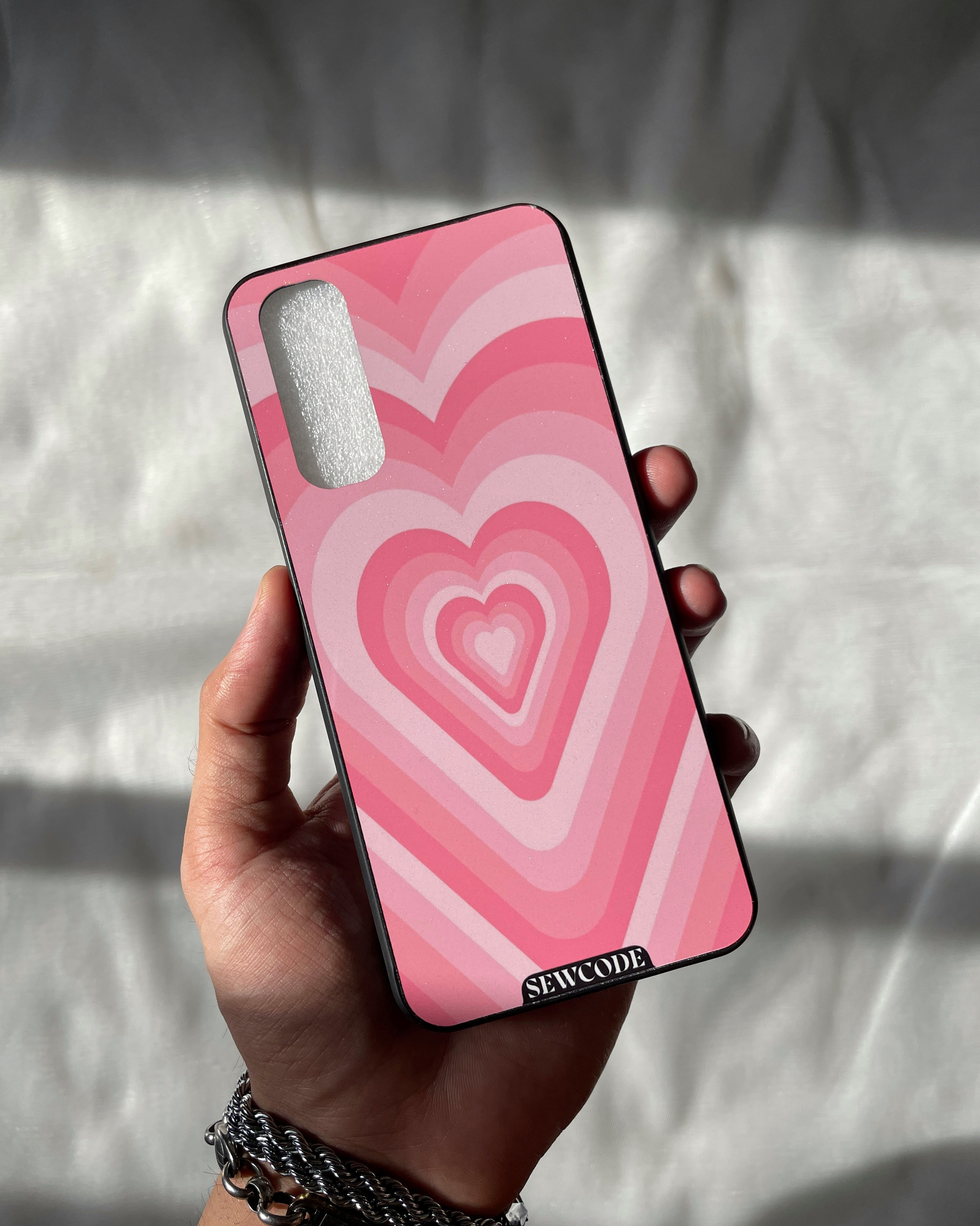 Hand holding a phone case with a concentric pink heart pattern, creating a tunnel effect.