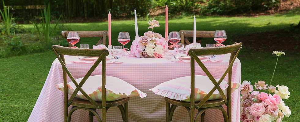 Eleganter, festlich gedeckter Tisch im Freien mit rosa karierter Tischdecke, passenden Servietten und stilvollen Kissenbezüge