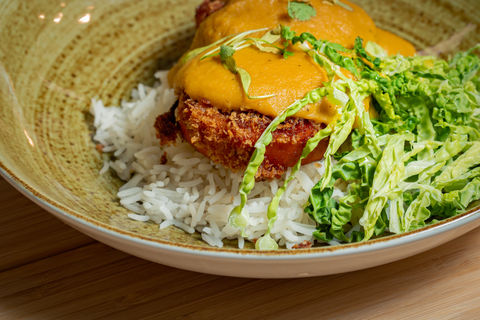 A breaded chicken breast served on a bed of fragrant rice and covered in katsu covered sauce with a side of cabbage, styled on wooden boards.