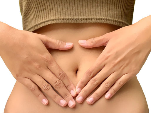 Hands placed on a bare abdomen below a beige ribbed top, suggesting comfort or self-care, on a plain background.
