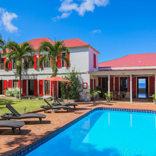 Blue pool, lounge chairs, palm trees, and the backside of the Main House of the Feather Leaf Inn, a Caribbean eco-hotel.
