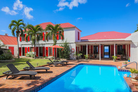 Blue pool, lounge chairs, palm trees, and the backside of the Main House of the Feather Leaf Inn, a Caribbean eco-hotel.
