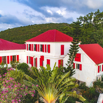 Aerial view of the Main House at the Feather Leaf Inn, a Caribbean eco-hotel, surrounded by green hills and flowers.