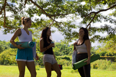 Three guests stand in a shaded grassy field with yoga mats at a plant-based retreat at the Feather Leaf Inn.