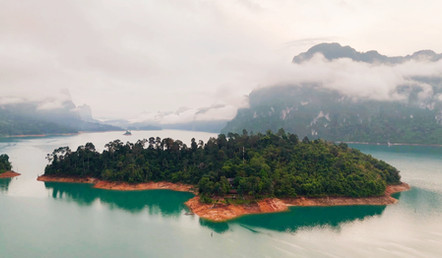 Remote island in Cheow Lan Lake surrounded by emerald water, limestone mountains, and morning mist in Khao Sok National Park.