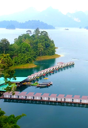 Aerial view of Phuphawaree Floating House surrounded by rainforest islands and emerald waters at Cheow Lan Lake in Khao Sok National Park
