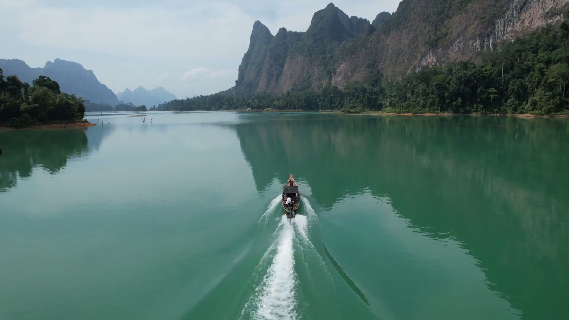 Traditional longtail boat traveling across Cheow Lan Lake toward remote rainforest waterways