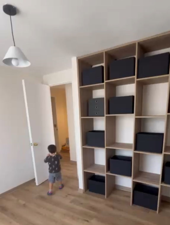 Niño entrando a una habitación con estantería y cajas negras. Atelier3ofcial