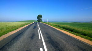 Empty rural road through green fields under blue sky, with Northeast Radio SD logo in the top left.