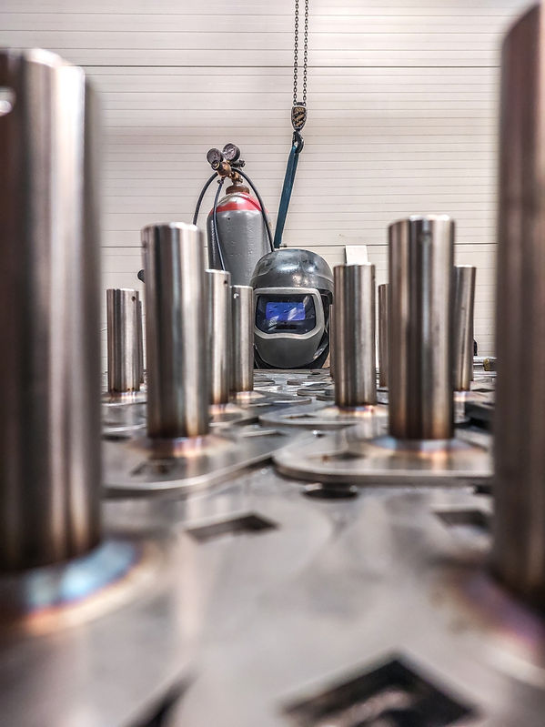 Personne portant un casque de soudure en train de travailler dans un environnement industriel, avec des outils et des équipements visibles